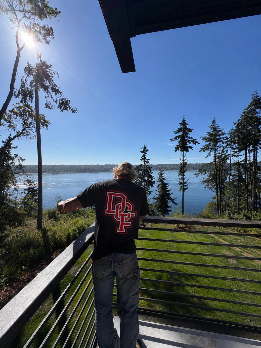 Dylan standing at a finished black horizontal-bar deck railing overlooking the water on a sunny day
