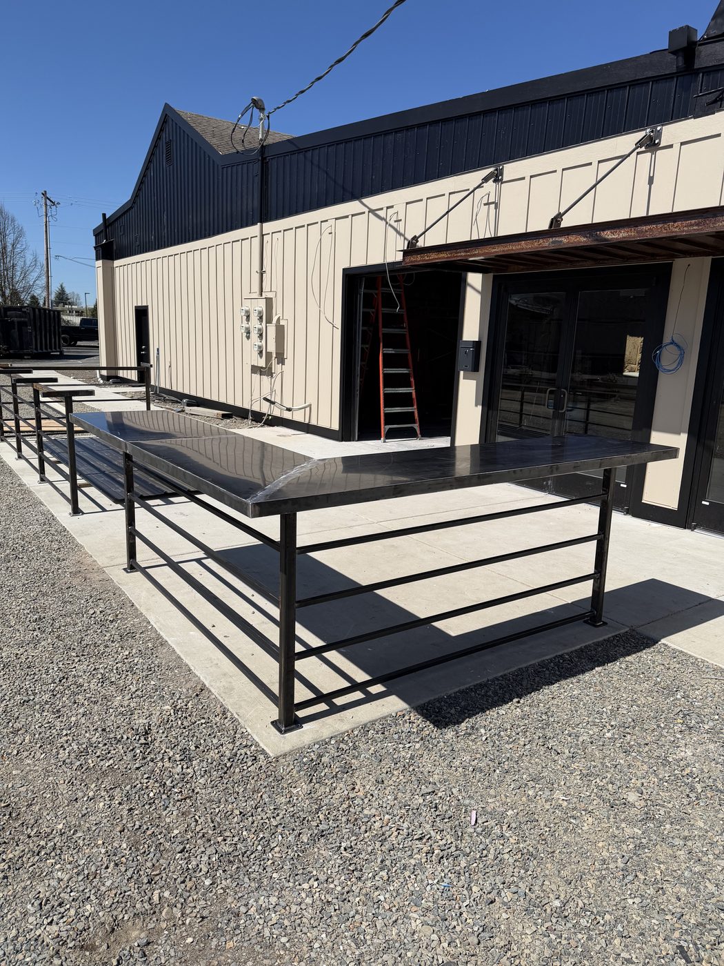 Outdoor horizontal-bar steel railing with a wide steel bar top along a commercial building
