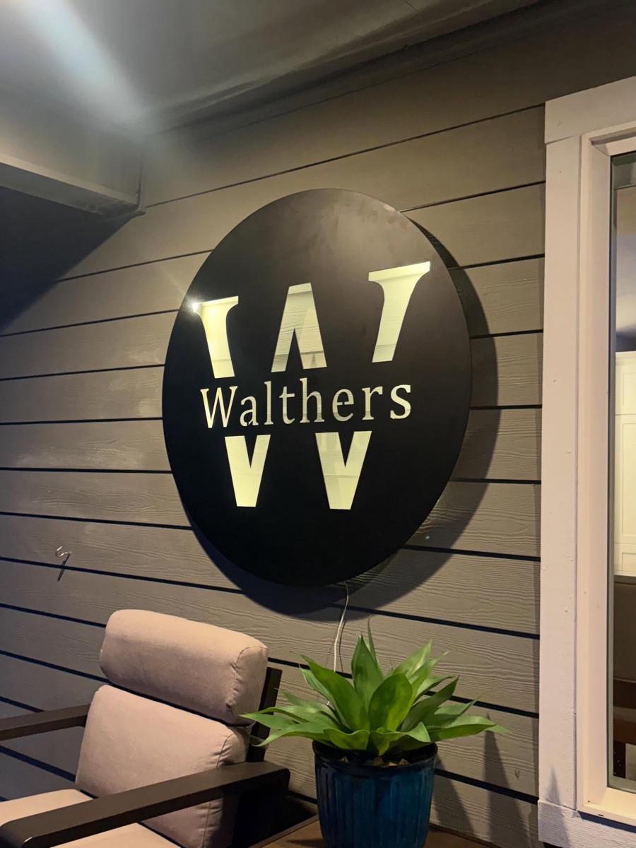 Circular backlit metal house sign with a W monogram on a wood-slat wall