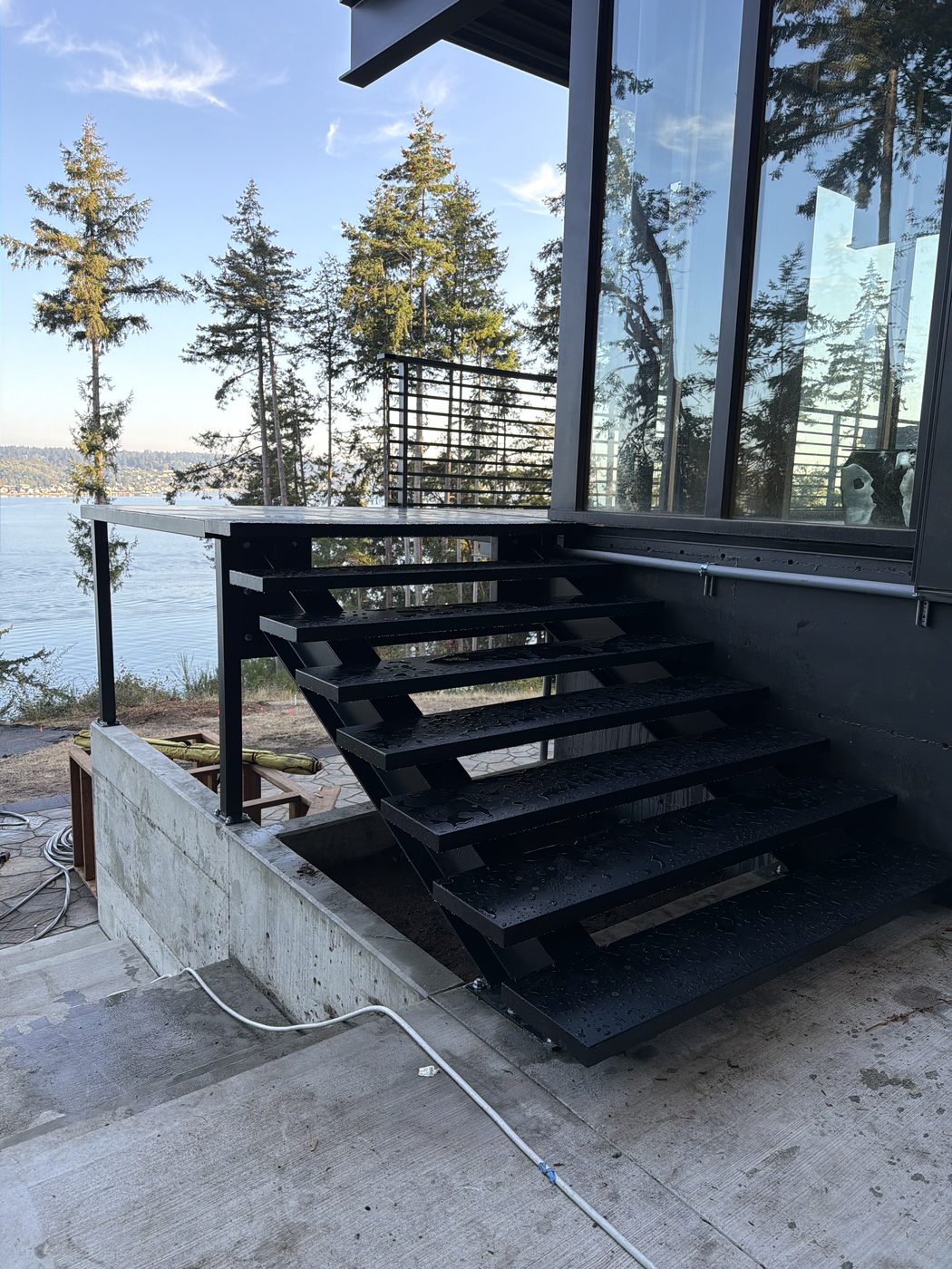 Open black steel staircase with a horizontal-bar rail at a modern waterfront home
