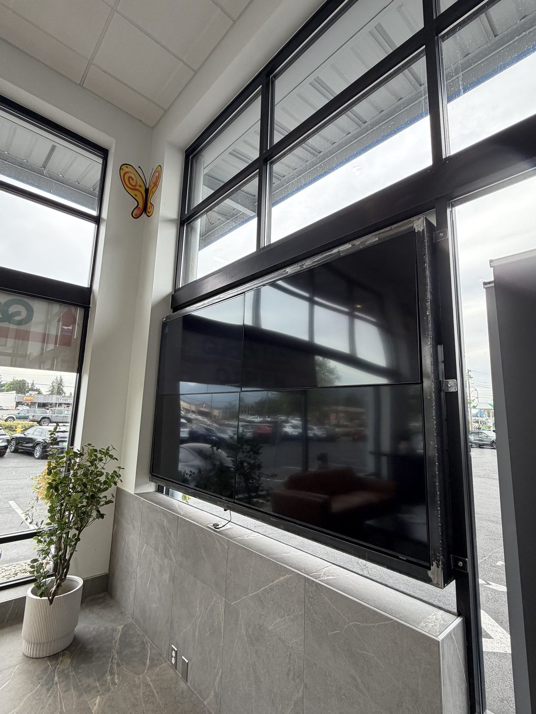 Large TV set in a custom black steel frame against a showroom window wall